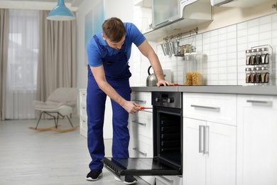 Professional serviceman repairing modern oven in kitchen