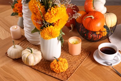 Autumn atmosphere. Beautiful bright orange flowers, pumpkins, cup of coffee and burning candles on wooden table