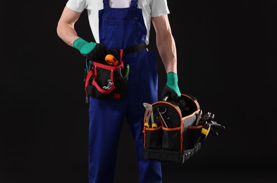 Professional repairman with tool box on black background