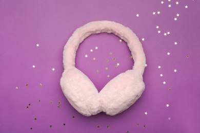 Photo of Stylish winter earmuffs and confetti on purple background, flat lay