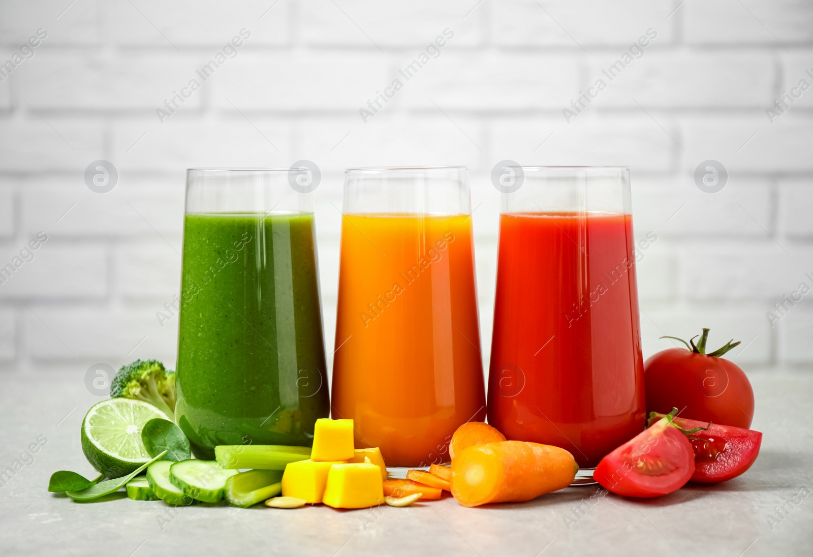 Photo of Different tasty juices and fresh ingredients on grey table against brick wall