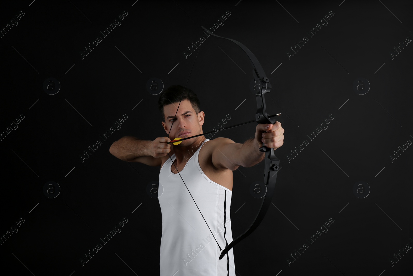 Photo of Man with bow and arrow practicing archery on black background