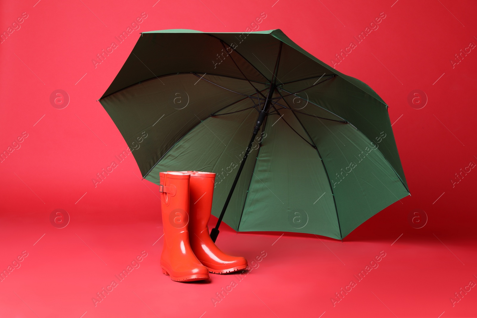 Photo of Open green umbrella and rubber boots on red background