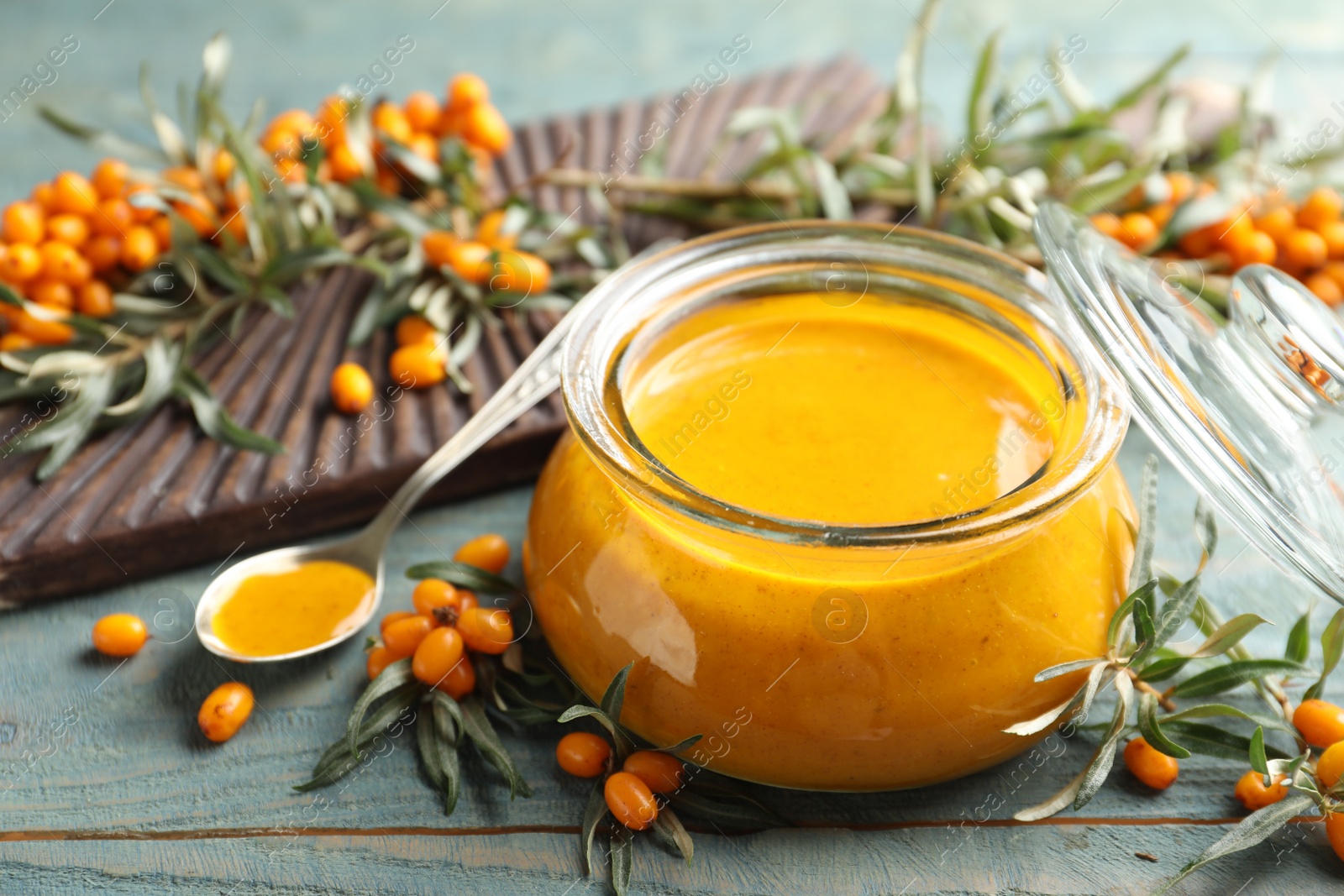 Photo of Delicious sea buckthorn jam and fresh berries on blue wooden table