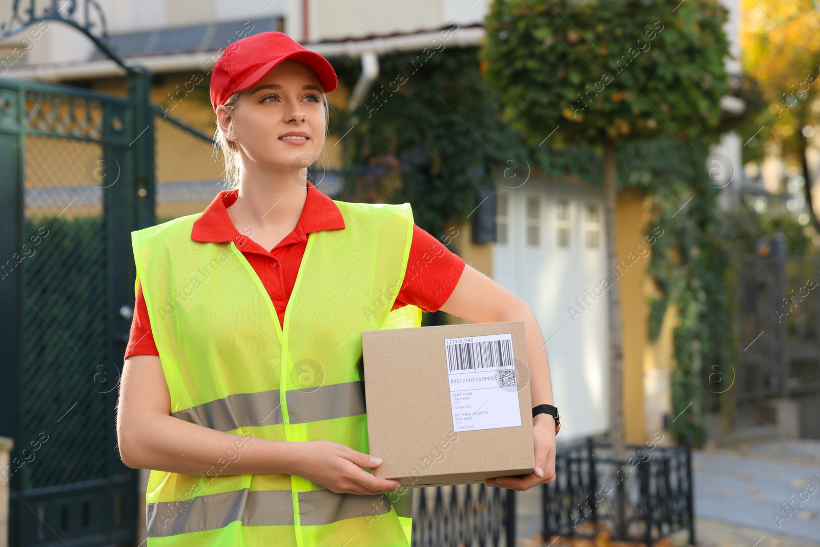 Photo of Courier in uniform with parcel near private house outdoors