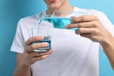 Young man using mouthwash on light blue background, closeup