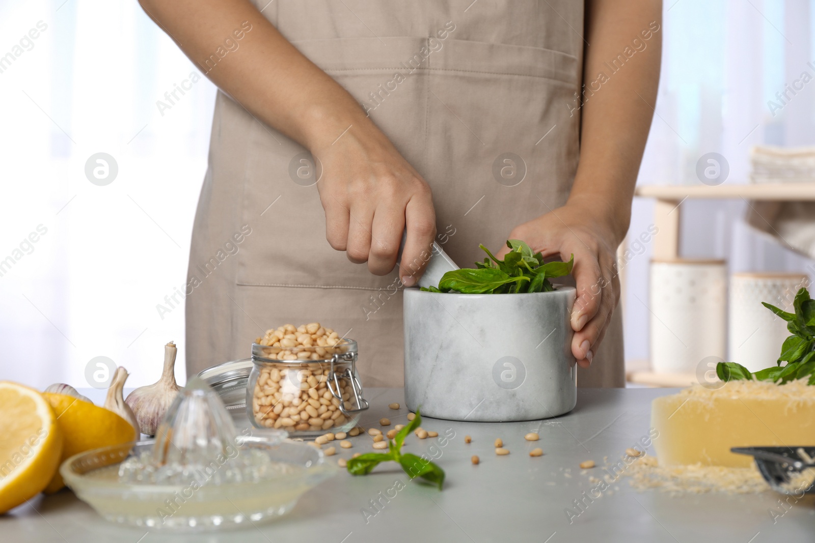 Photo of Woman making basil pesto sauce at kitchen table