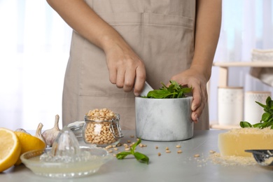 Photo of Woman making basil pesto sauce at kitchen table