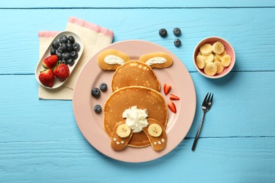 Creative serving for kids. Plate with cute bunny made of pancakes, berries, cream and banana on light blue wooden table, flat lay