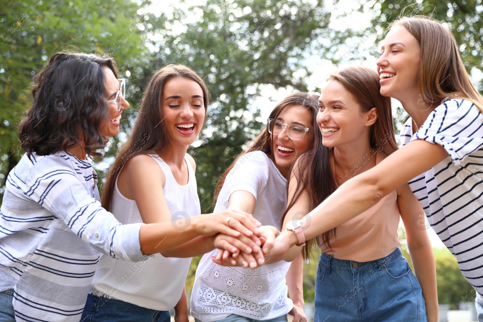 Photo of Happy women putting hands together outdoors on sunny day. Girl power concept