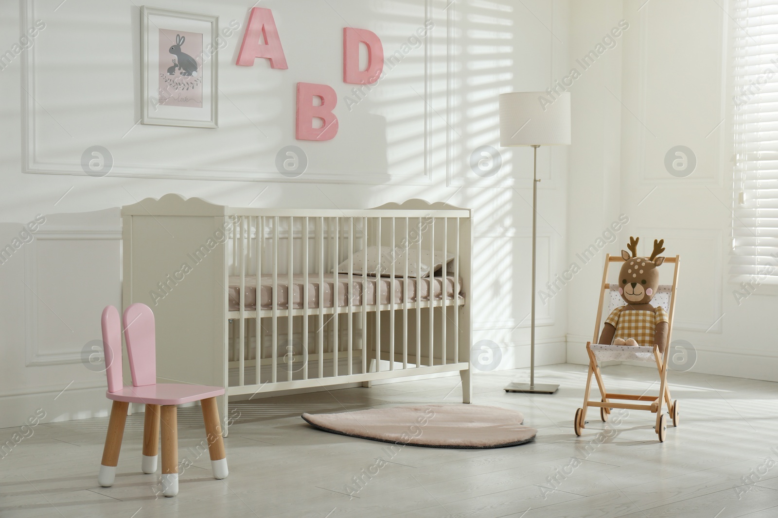 Photo of Comfortable crib near wall with pink letters in baby room. Interior design