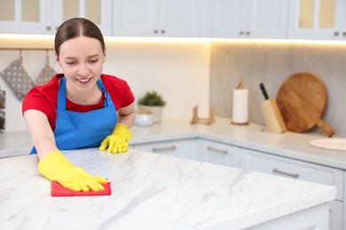 Photo of Woman cleaning white marble table with rag in kitchen, space for text