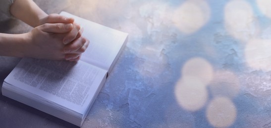 Image of Religion. Christian woman praying over Bible at table, closeup. Bokeh effect. Banner design