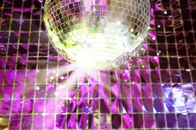 Image of Shiny disco ball against foil party curtain, low angle view. Bokeh effect