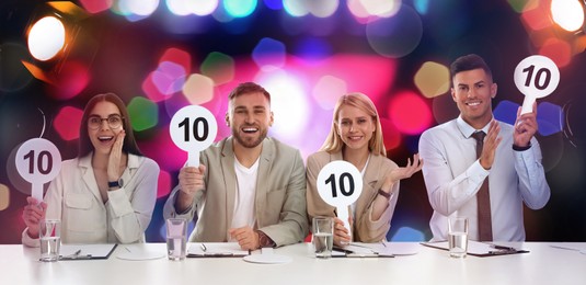 Image of Panel of judges holding signs with highest score at table against blurred background. Bokeh effect