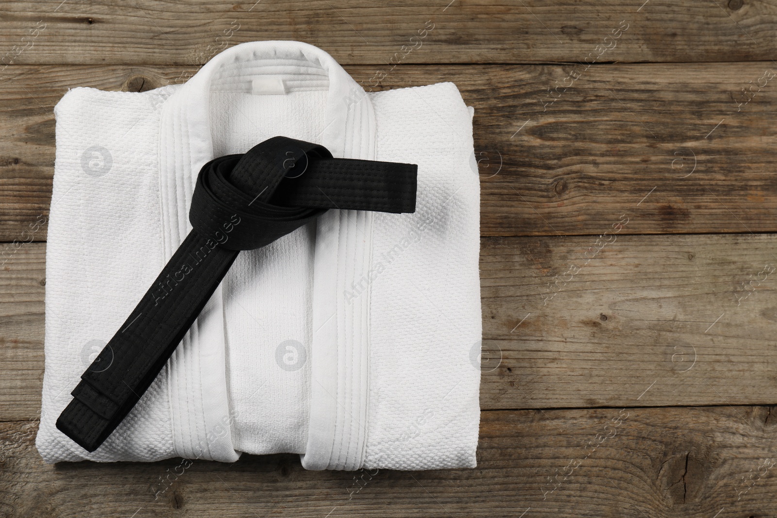 Photo of Black karate belt and white kimono on wooden background, top view. Space for text