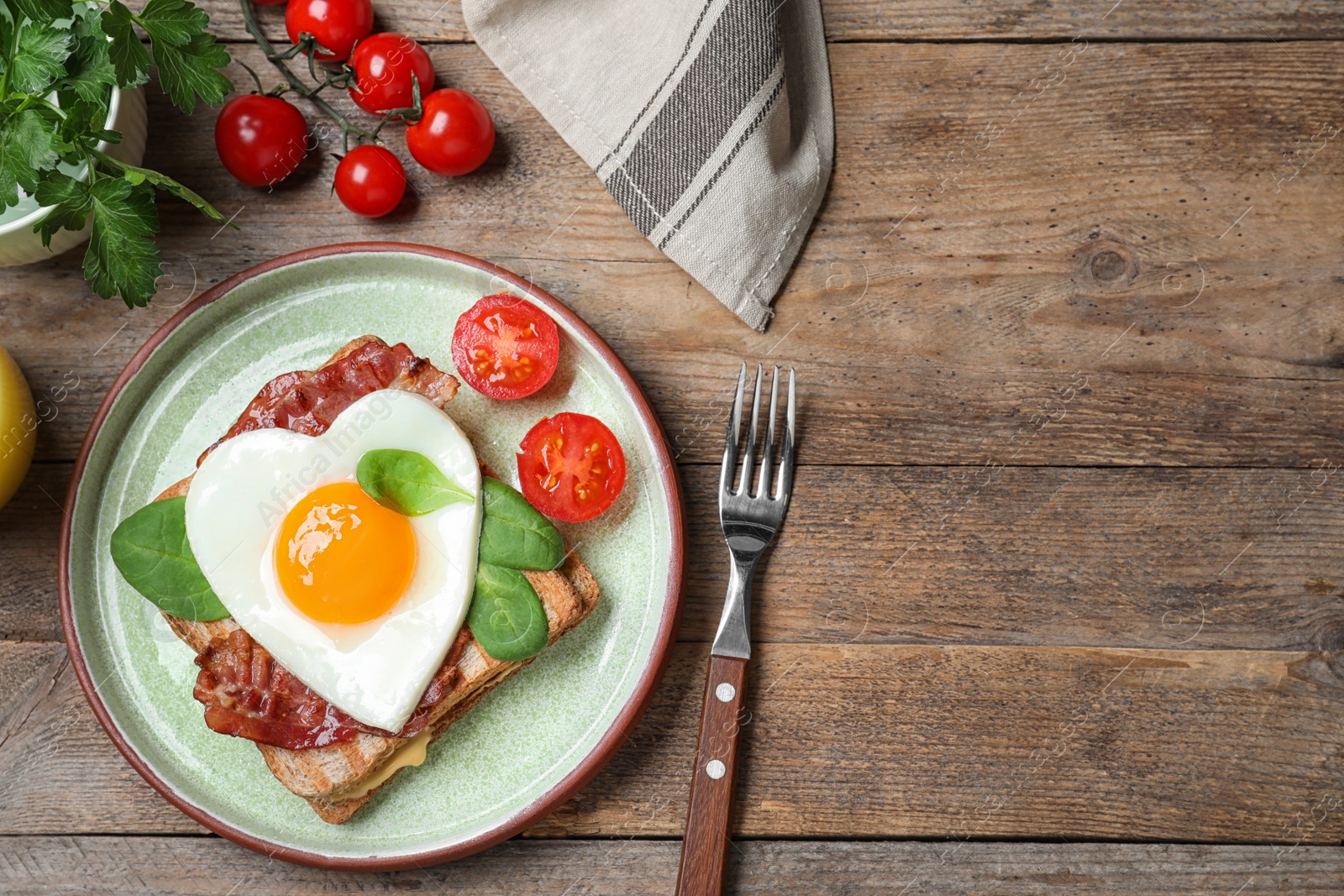 Photo of Tasty sandwich with heart shaped fried egg and bacon on wooden table, flat lay. Space for text