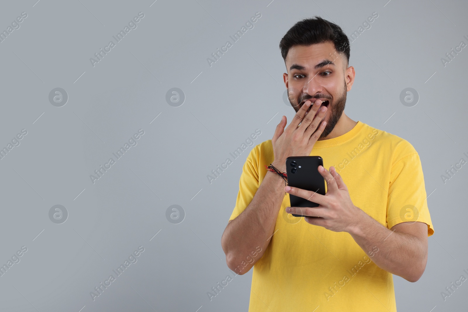 Photo of Handsome young man using smartphone on grey background, space for text