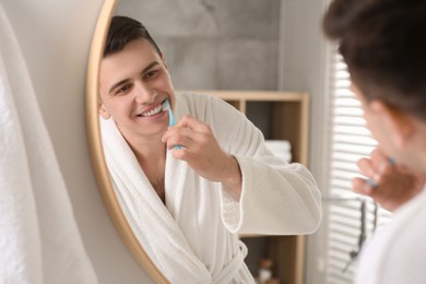 Man brushing his teeth with toothbrush near mirror in bathroom