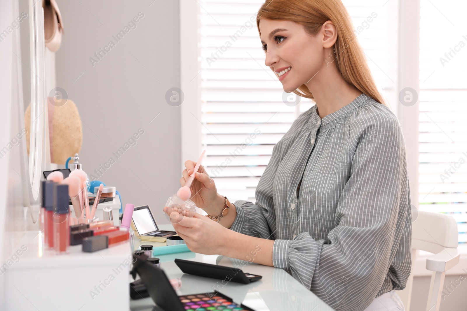 Photo of Beautiful young woman applying makeup near mirror in dressing room