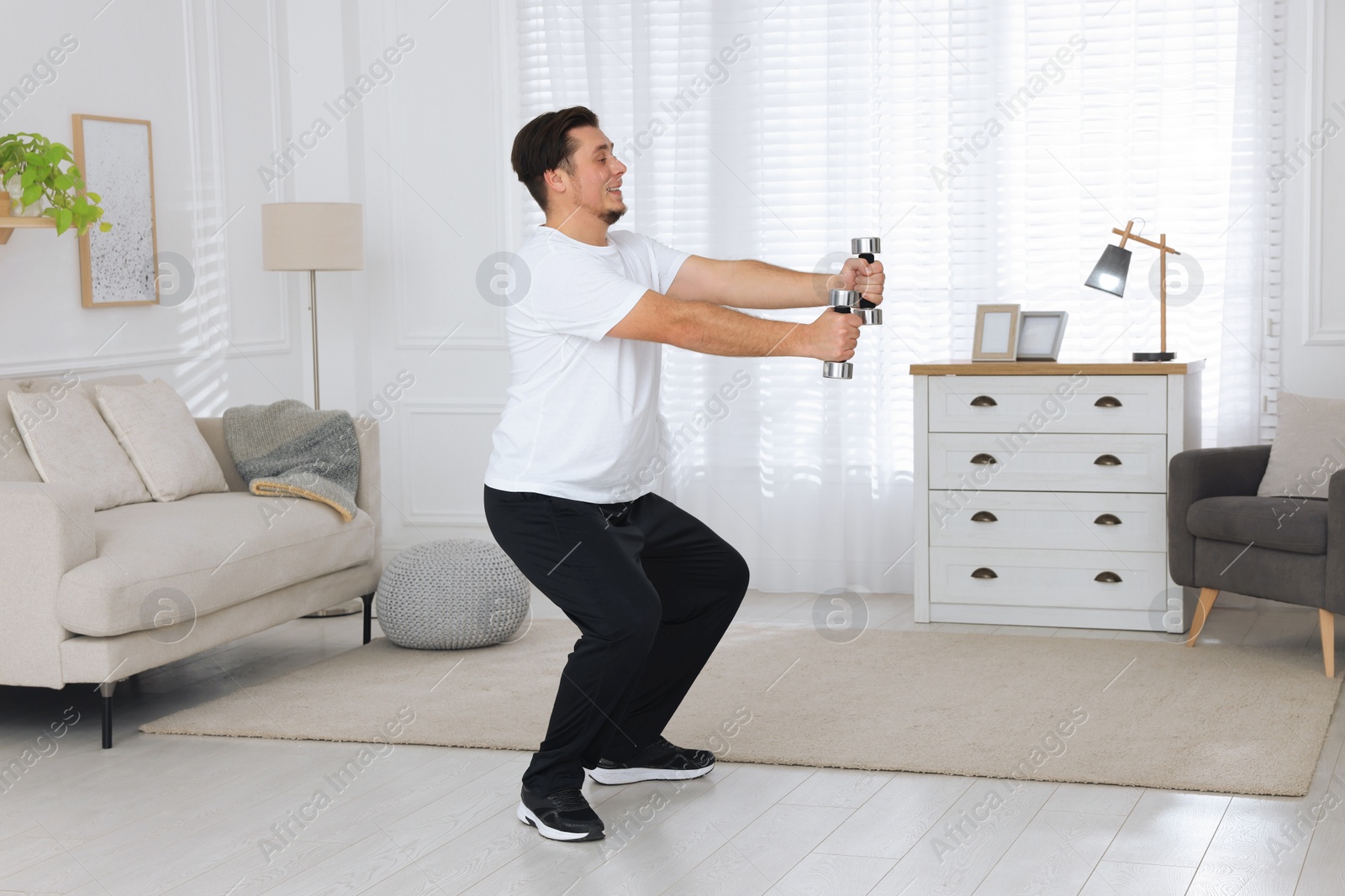 Photo of Overweight man doing squat exercise with dumbbells at home