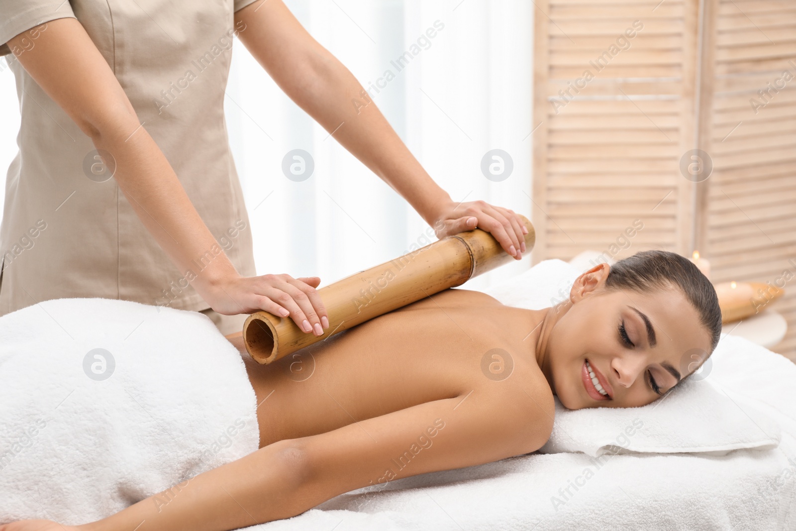 Photo of Young woman having massage with bamboo stick in wellness center