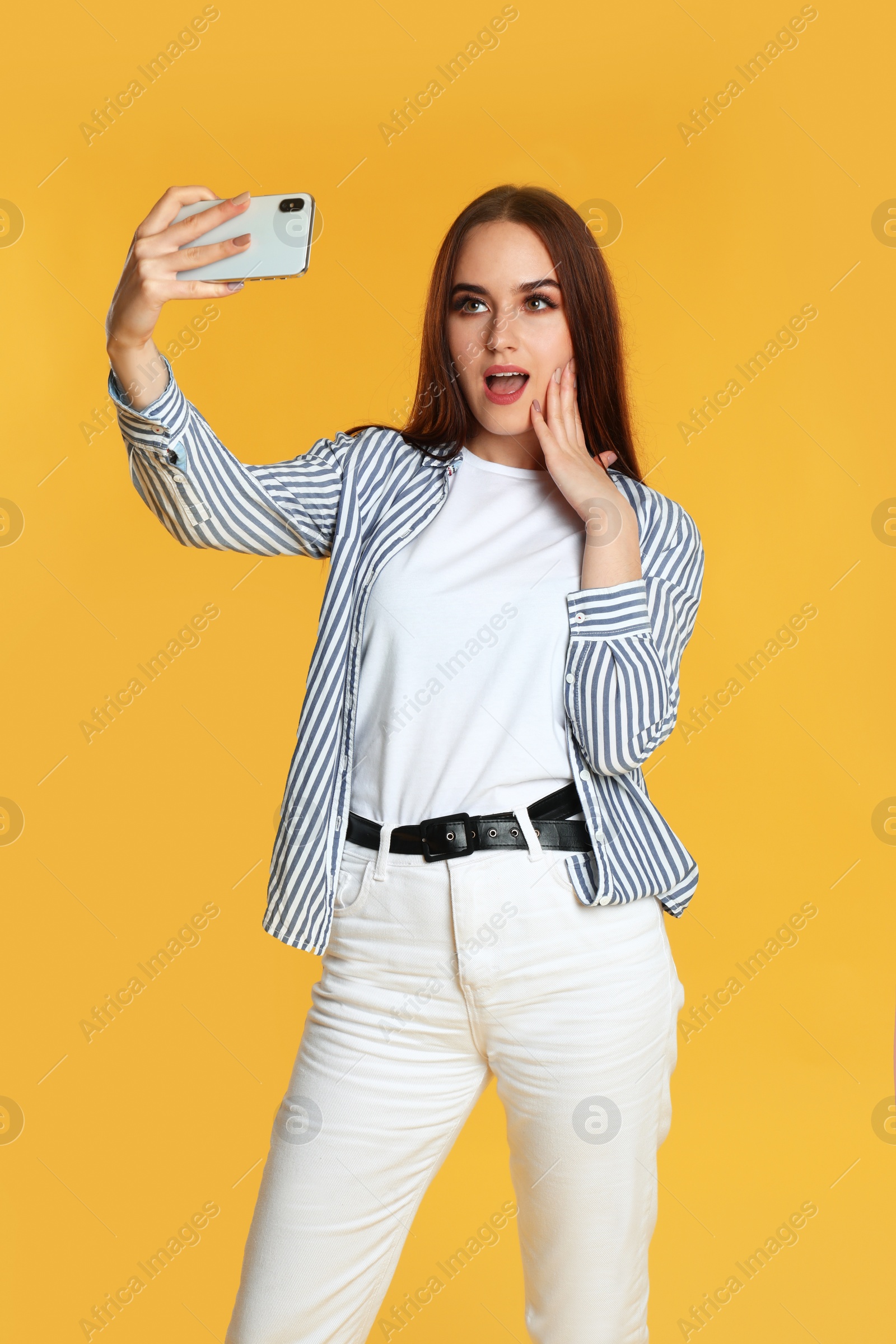 Photo of Young woman taking selfie on yellow background