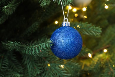 Photo of Beautiful blue Christmas ball hanging on fir tree branch, closeup