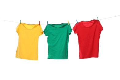 Photo of Different bright t-shirts drying on washing line against white background