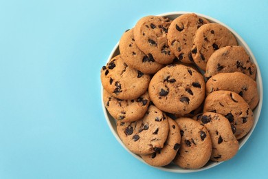 Photo of Bowl of delicious chocolate chip cookies on light blue background, top view. Space for text
