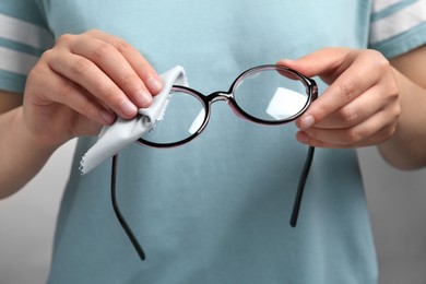 Photo of Woman wiping glasses with microfiber cloth on light grey background, closeup