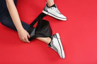 Photo of Woman in stylish shoes with bum bag sitting on color background