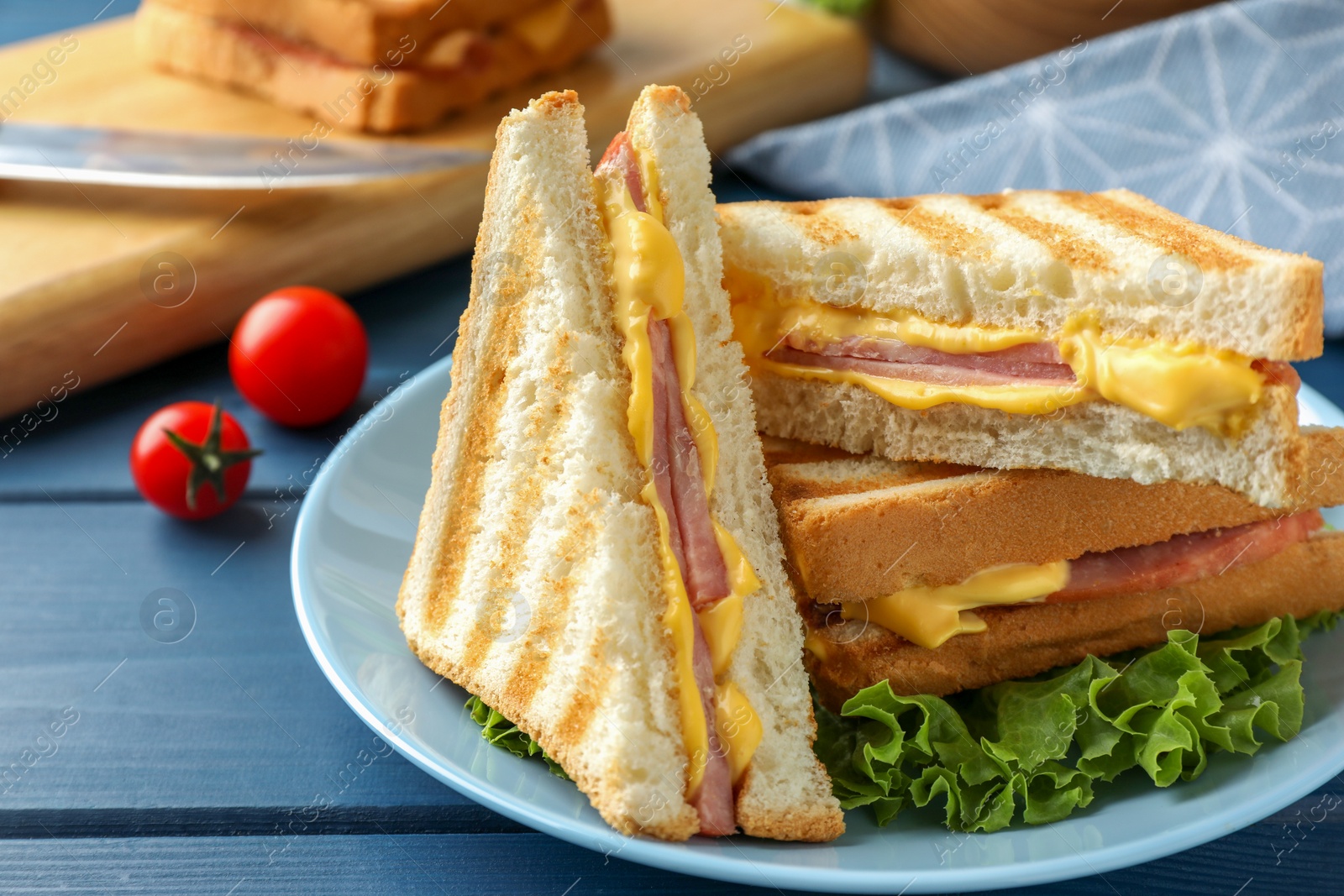 Photo of Tasty sandwiches with ham, melted cheese and lettuce on blue wooden table, closeup