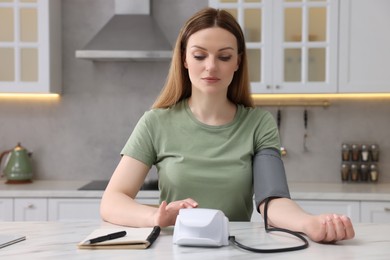 Photo of Woman measuring blood pressure with tonometer in kitchen