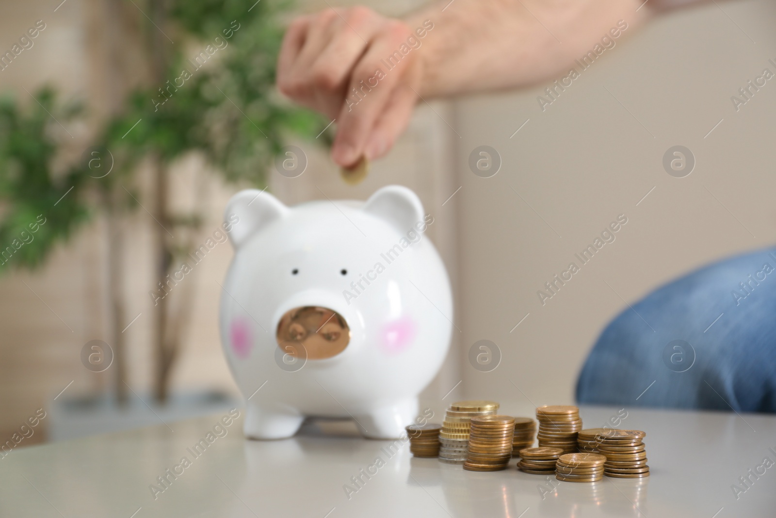 Photo of Man putting coin into piggy bank at table indoors, selective focus. Money saving