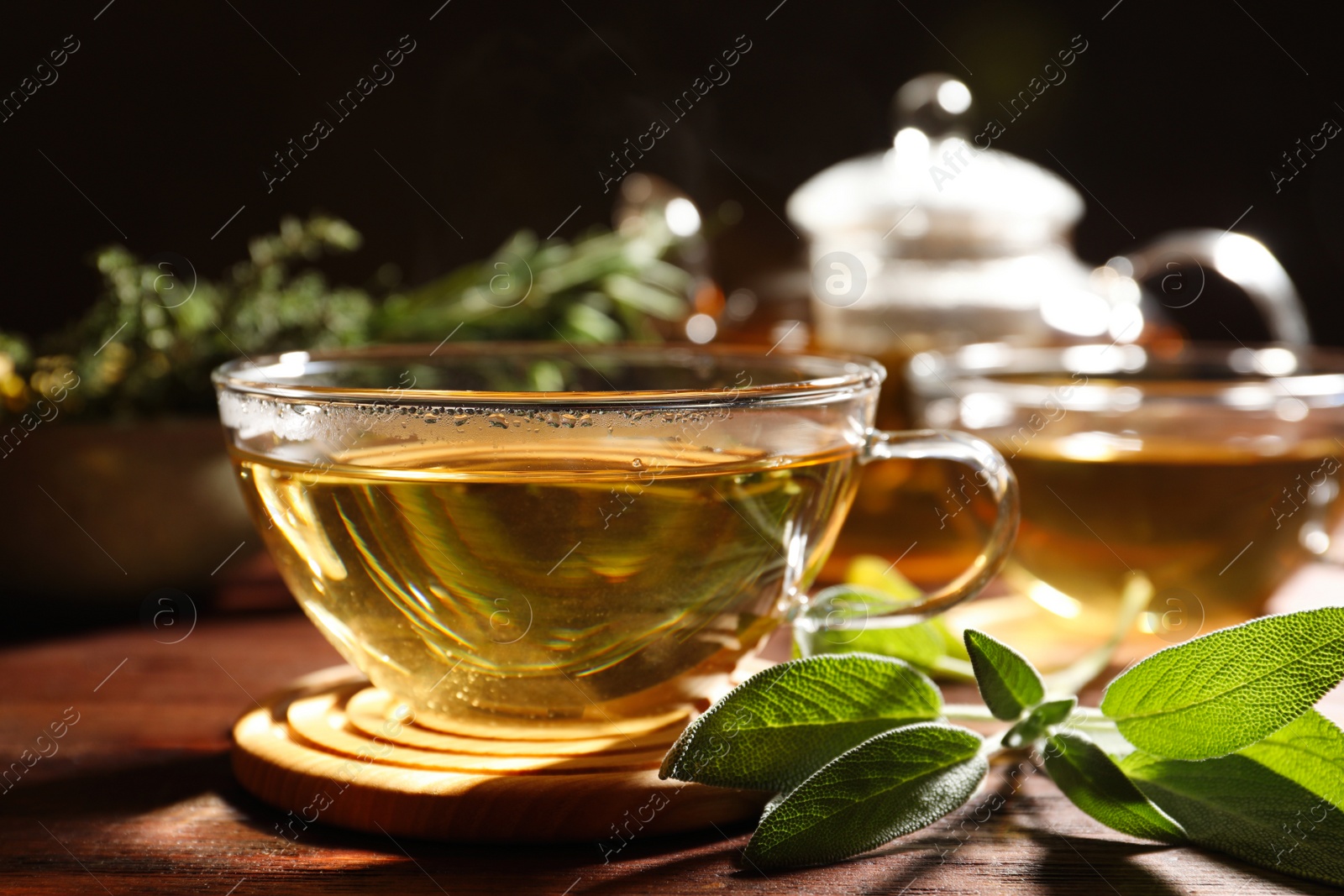 Photo of Cup of aromatic herbal tea and fresh sage on wooden table, closeup