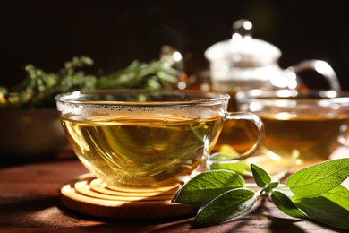 Cup of aromatic herbal tea and fresh sage on wooden table, closeup