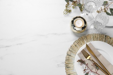 Stylish setting with cutlery, burning candle and eucalyptus leaves on white marble table, flat lay. Space for text