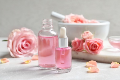 Photo of Bottles of rose essential oil and fresh flowers on table