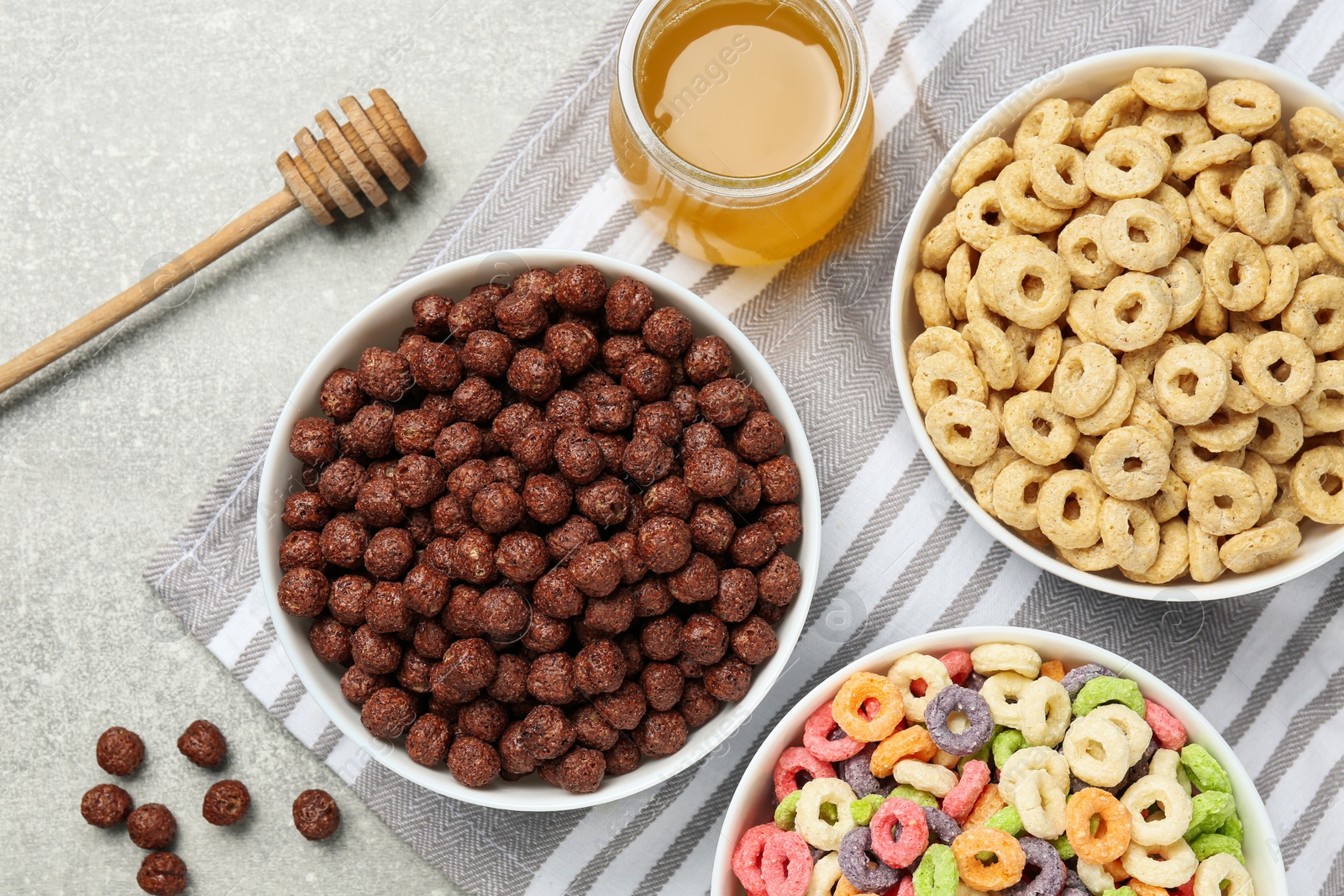 Photo of Different delicious breakfast cereals and honey on light grey table, flat lay