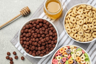 Different delicious breakfast cereals and honey on light grey table, flat lay