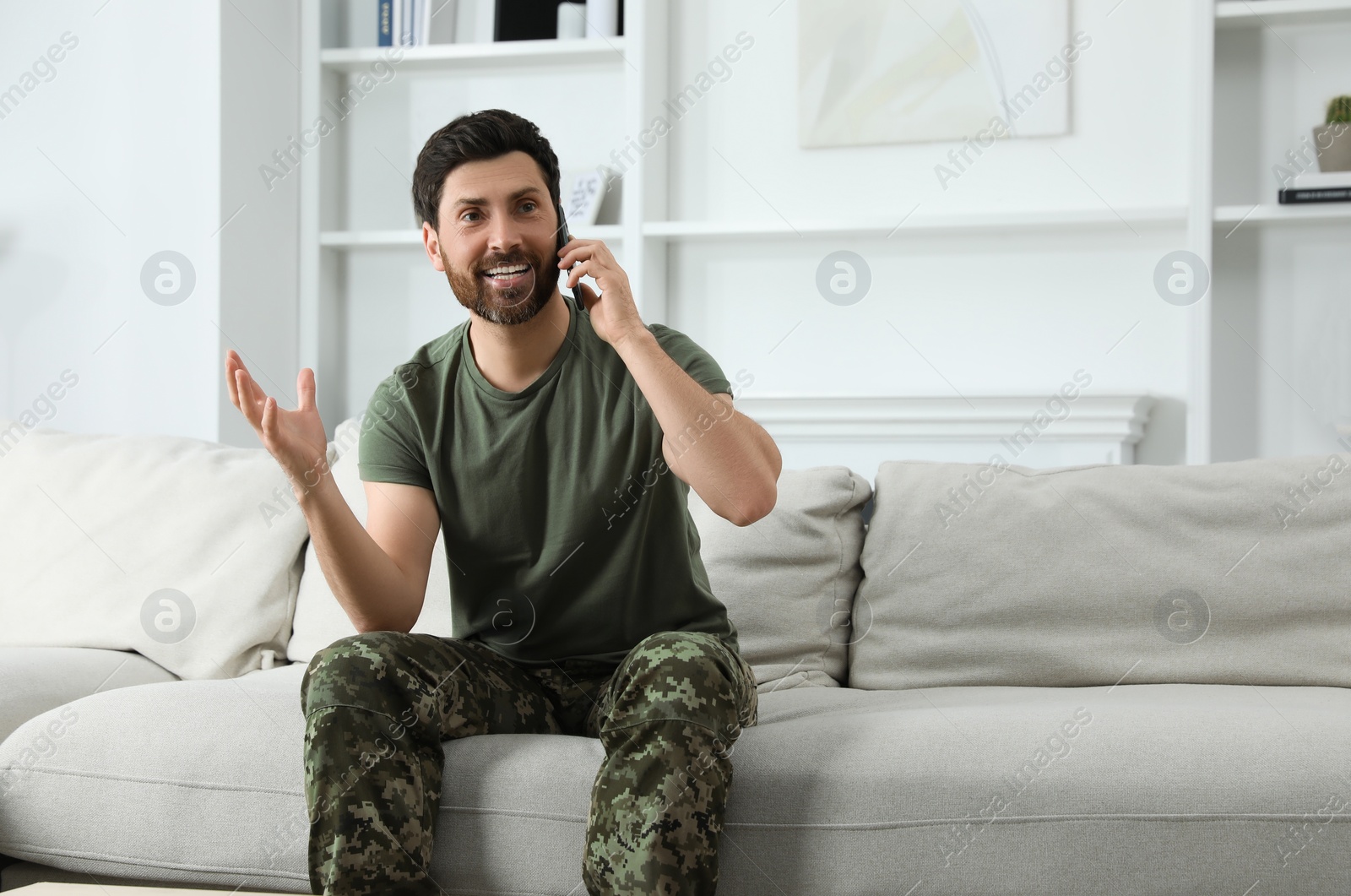 Photo of Happy soldier talking on phone in living room. Military service