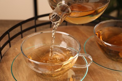 Photo of Pouring tasty tea into glass cup at wooden table, closeup