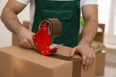 Photo of Man packing box with adhesive tape indoors, closeup. Moving service