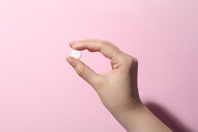Woman holding pill on pink background, closeup