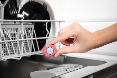Photo of Woman putting detergent tablet into open dishwasher in kitchen, closeup