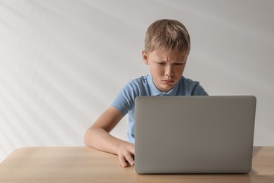 Upset boy with laptop at table, space for text. Cyber bullying