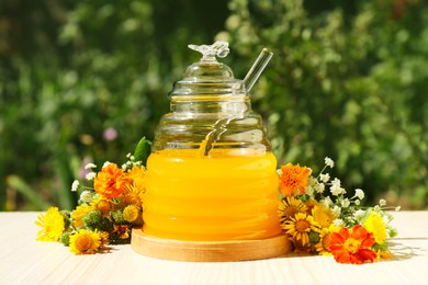 Delicious fresh honey and beautiful flowers on wooden table in garden