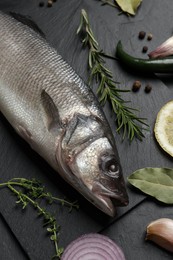 Photo of Sea bass fish and ingredients on black table, closeup