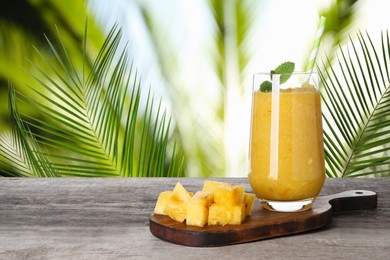 Image of Tasty pineapple smoothie in glass on wooden table against blurred background, space for text